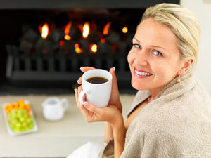 Woman drinking a coffee in front of her fireplace in the living.